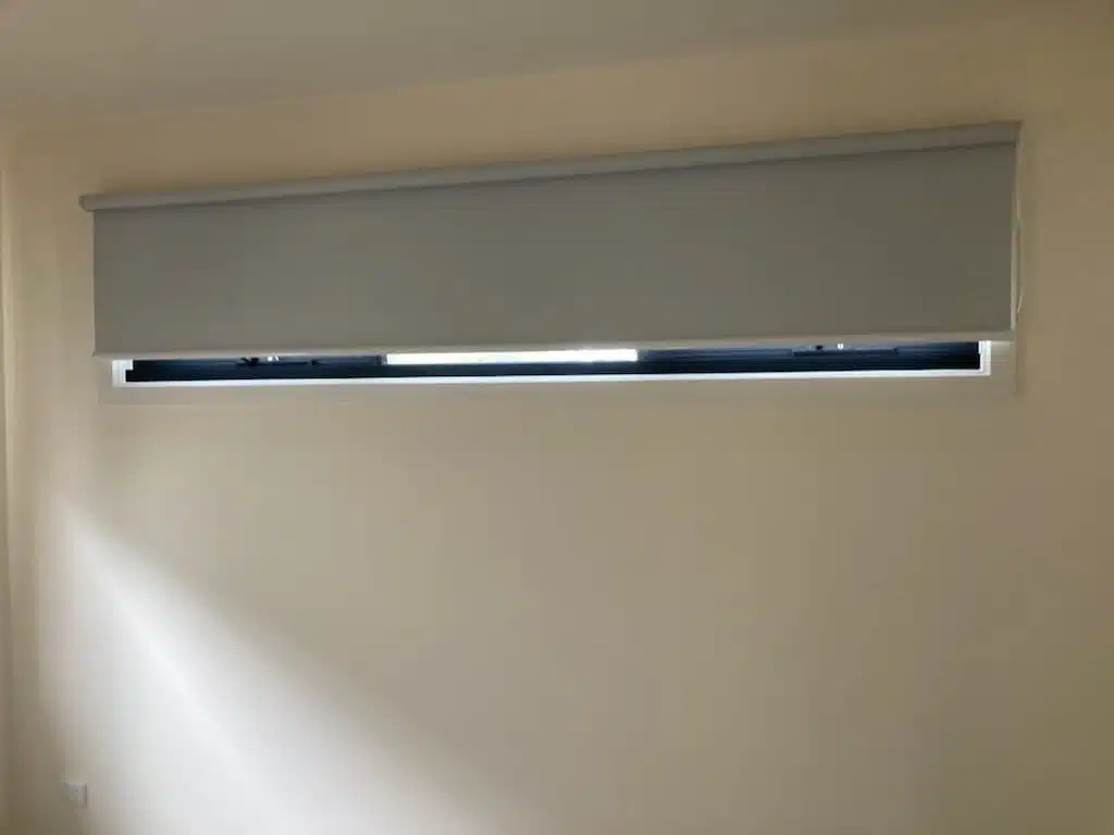 Wide grey roller blind fitted above a horizontal window